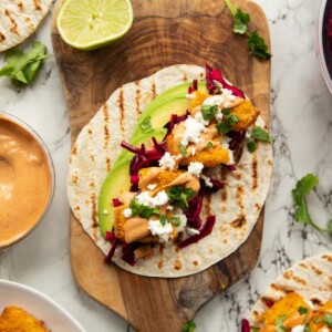 overhead shot of fish finger taco on wooden board surrounded by garnish