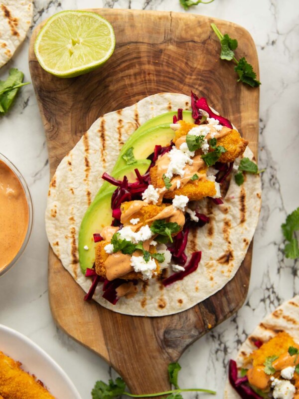 overhead shot of fish finger taco on wooden board surrounded by garnish