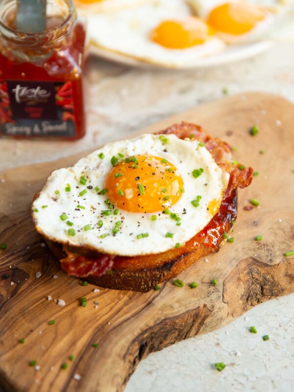 fried egg on toast on wooden board with chilli jam and fried eggs blurred in background