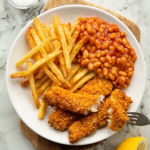 overhead shot of fish fingers, chips and beans on small white plate