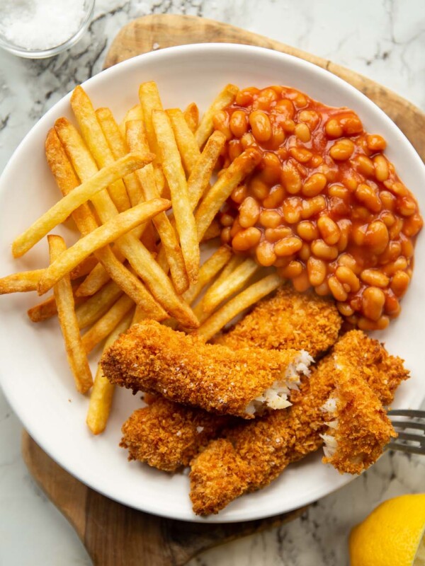 overhead shot of fish fingers, chips and beans on small white plate