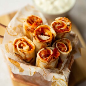 6 pizza roll ups in a small pot with dip blurred in the background