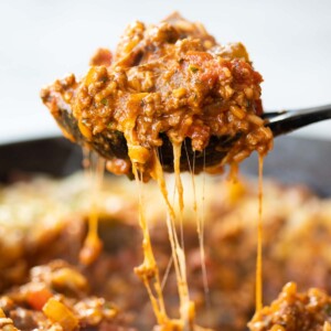 side shot of black serving spoon scooping unstuffed peppers out of cast iron skillet with cheese dripping down