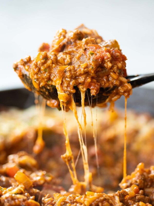 side shot of black serving spoon scooping unstuffed peppers out of cast iron skillet with cheese dripping down