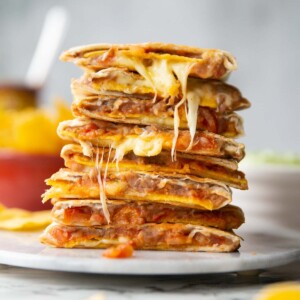 8 refried bean quesadillas halves stacked on each other on marble plate with ingredients blurred in background