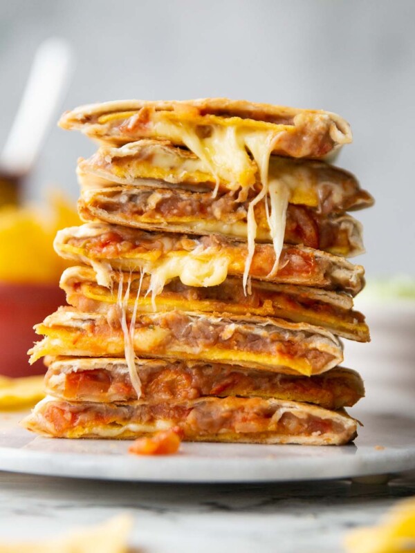 8 refried bean quesadillas halves stacked on each other on marble plate with ingredients blurred in background