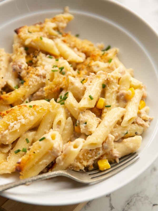 close up shot of creamy tuna pasta bake in white bowl with silver fork digging in