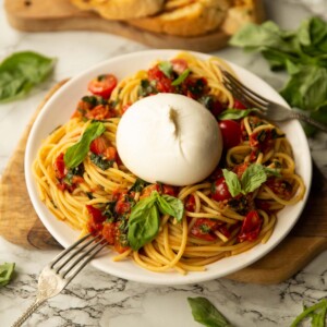 side shot of burrata caprese pasta on small white plate garnished with fresh basil