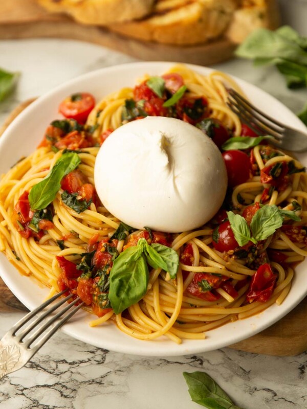 side shot of burrata caprese pasta on small white plate garnished with fresh basil