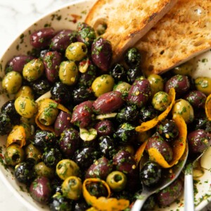 close up shot of large white dish with marinated olives and two slices of toasted ciabatta