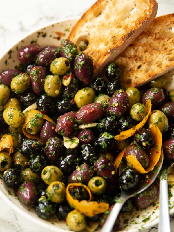 close up shot of large white dish with marinated olives and two slices of toasted ciabatta