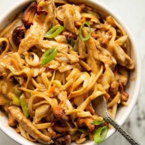 close up overhead shot of cashew butter chicken noodles in small with bowl with silver fork digging in