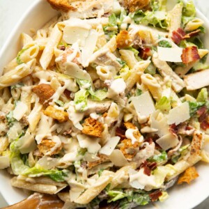 close up overhead shot of chicken caesar pasta salad in large white bowl with wooden salad tossers