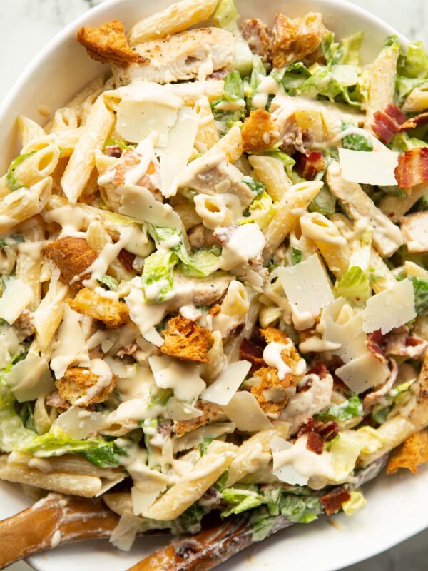 close up overhead shot of chicken caesar pasta salad in large white bowl with wooden salad tossers