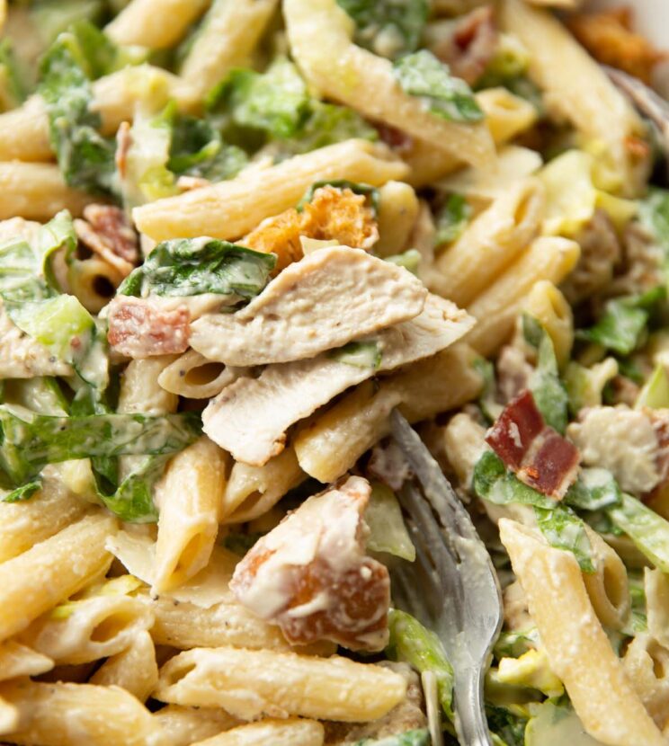 close up shot of fork stabbing into bowl of chicken caesar pasta salad