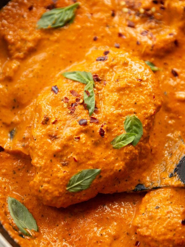 close up shot of creamy roasted red pepper chicken in large pan with spatula lifting chicken