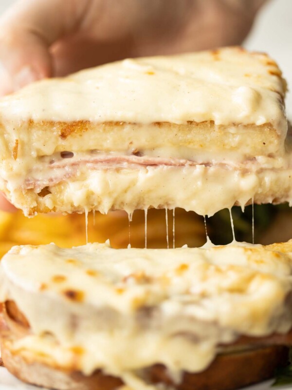 close up shot of hand lifting half of croque monsieur showing filling