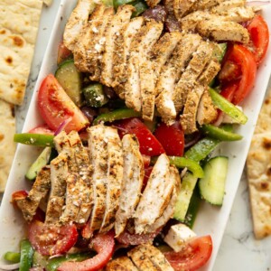 overhead shot of greek chicken salad served on large rectangular white dish surround by flatbread