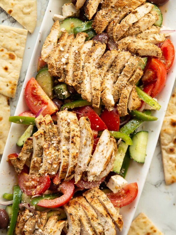 overhead shot of greek chicken salad served on large rectangular white dish surround by flatbread