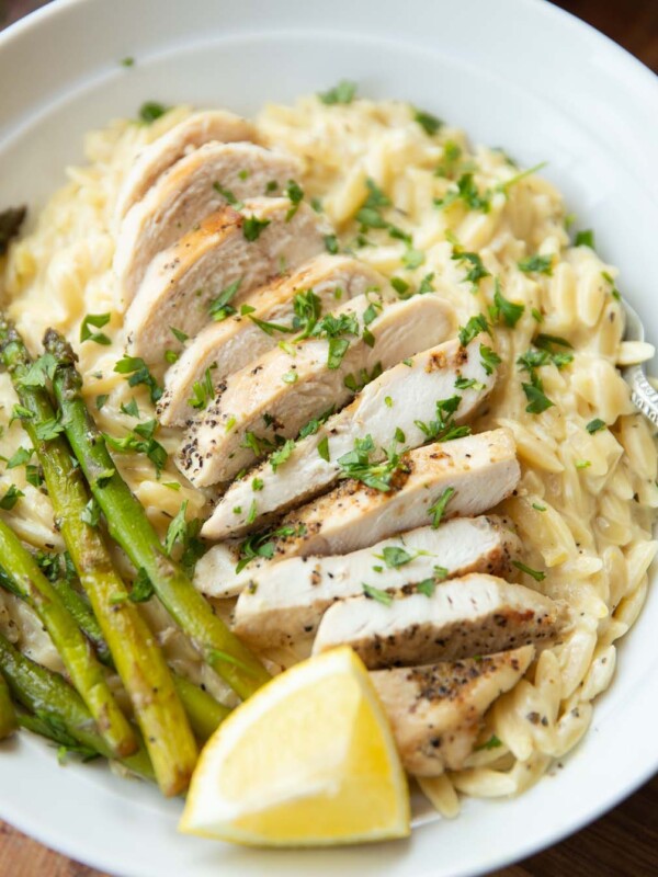 close up shot of lemon chicken orzo served in white bowl garnished with fresh parsley