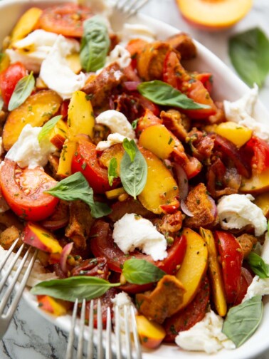 close up shot of peach tomato salad in large white dish garnished with fresh basil