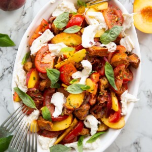 overhead shot of tomato peach salad in large white dish garnished with fresh basil