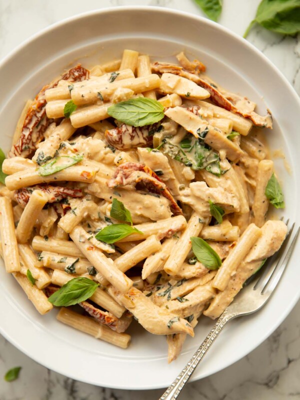 overhead shot of chicken sun dried tomato pasta in white dish with silver fork garnished with fresh basil