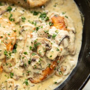 close up shot of creamy mushroom garlic chicken in cast iron skillet garnished with parsley