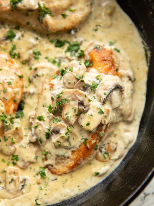 close up shot of creamy mushroom garlic chicken in cast iron skillet garnished with parsley