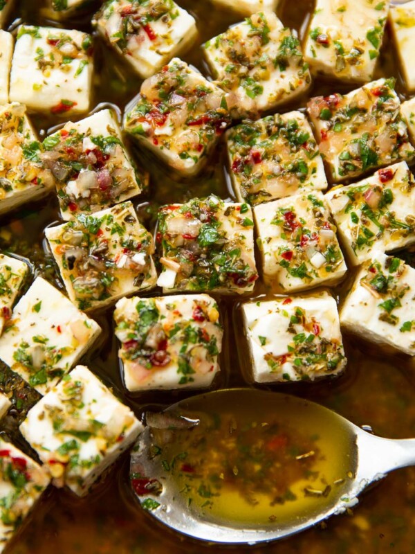 close up shot of marinated feta in glass dish with silver spoon