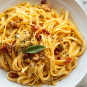 close up shot of roasted butternut squash pasta in white bowl garnished with fresh sage