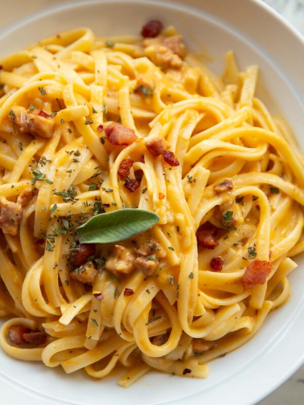 close up shot of roasted butternut squash pasta in white bowl garnished with fresh sage