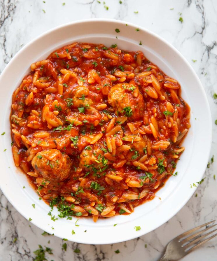 overhead shot of meatballs and orzo in a large white bowl on a marble backdrop garnished with fresh parsley