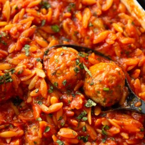 close up shot of black serving spoon scooping two meatballs out of dish of orzo