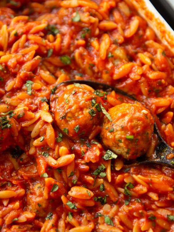 close up shot of black serving spoon scooping two meatballs out of dish of orzo