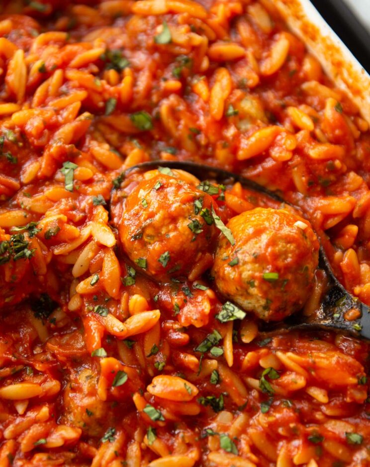 close up shot of black serving spoon scooping two meatballs out of dish of orzo