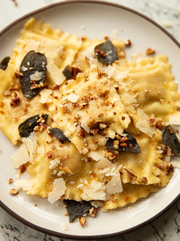 close up shot of ravioli on small white plate garnished with crispy sage, pecans and parmesan