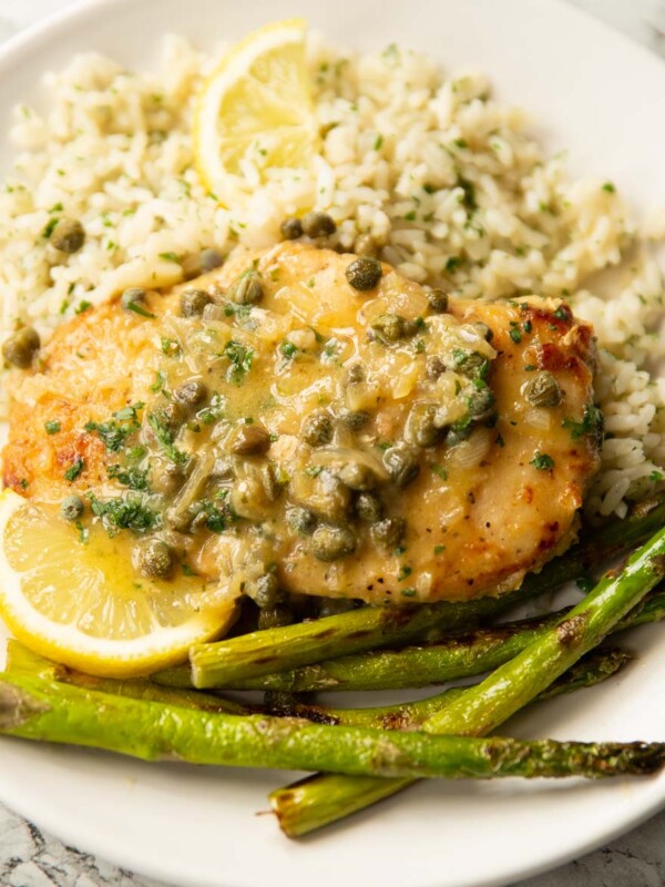 chicken piccata served on small white plate with rice, asparagus and lemon wedges