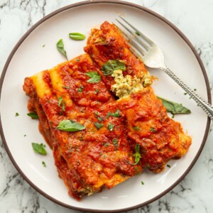 overhead shot of 3 ricotta pesto cannelloni on small white plate with silver fork on marble background