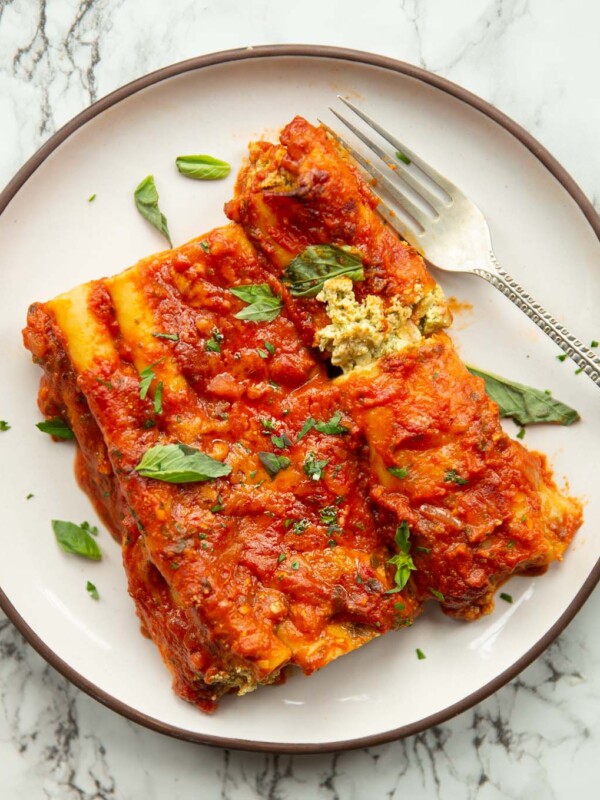 overhead shot of 3 ricotta pesto cannelloni on small white plate with silver fork on marble background