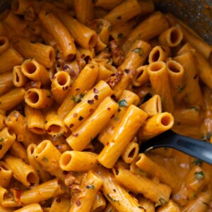 overhead shot of black serving spoon digging into pot of spicy rigatoni