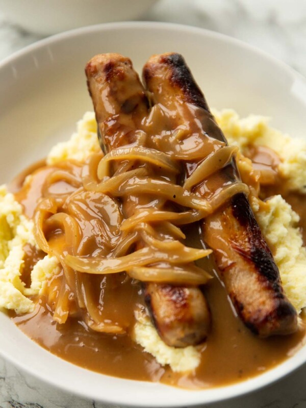 2 sausages on a bed of mashed potatoes with onion gravy in large white bowl