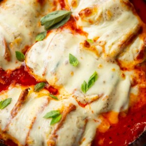 close up shot of hasselback chicken in skillet fresh out the oven garnished with fresh basil