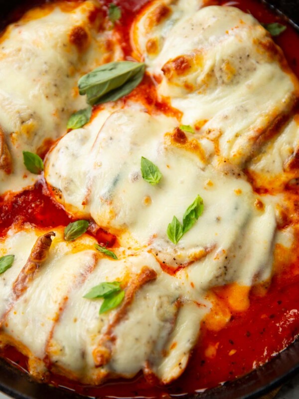 close up shot of hasselback chicken in skillet fresh out the oven garnished with fresh basil