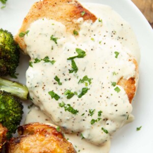 close up overhead shot of chicken breast and creamy garlic sauce on white plate with broccoli and smashed potatoes