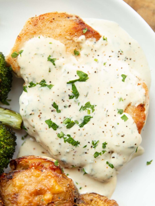 close up overhead shot of chicken breast and creamy garlic sauce on white plate with broccoli and smashed potatoes