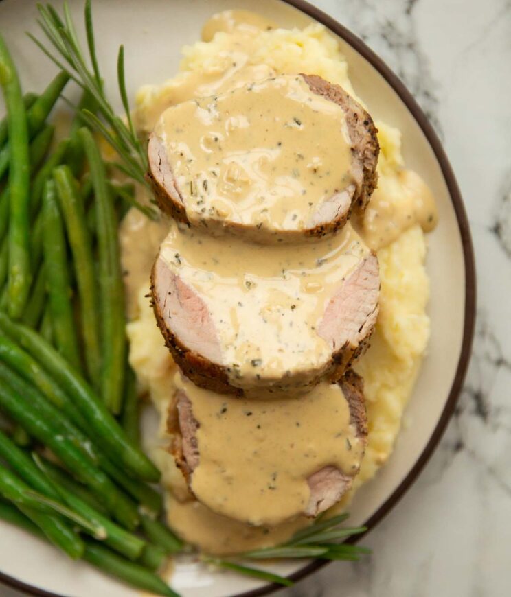 overhead close up shot of 3 slices of pork tenderloin on mashed potato with creamy mustard sauce