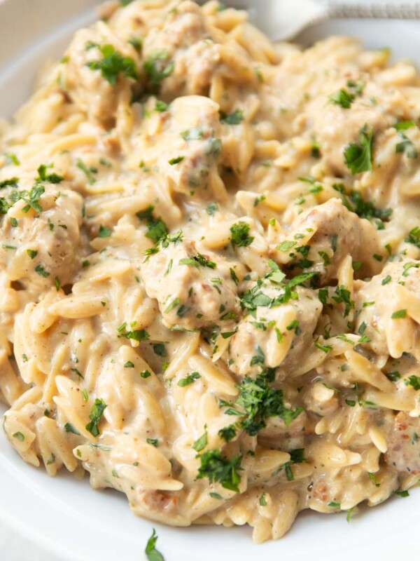 close up shot of garlic parmesan sausage orzo in small white bowl garnished with parsley