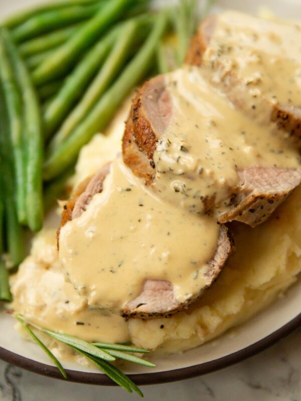 close up shot of pork tenderloin slices on mashed potato with mustard sauce and green beans blurred in background