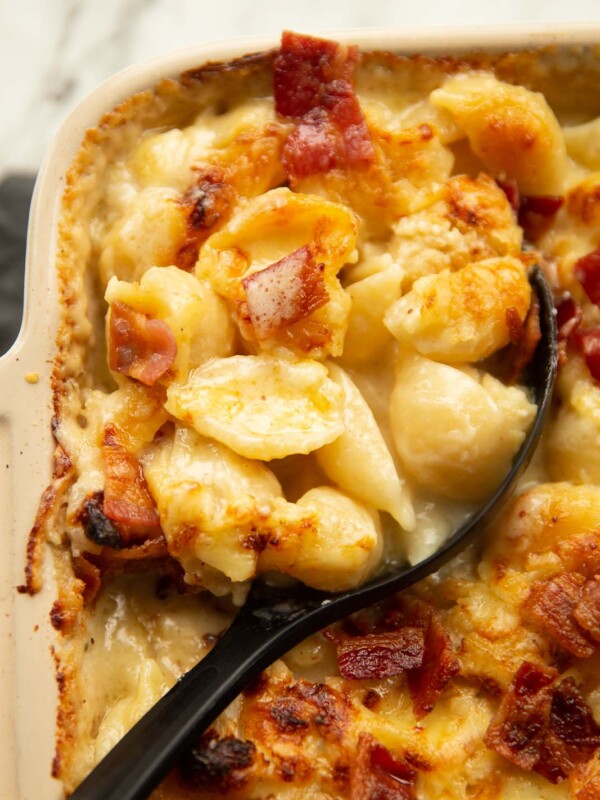 close up shot of cauliflower cheese pasta bake with black serving spoon digging in